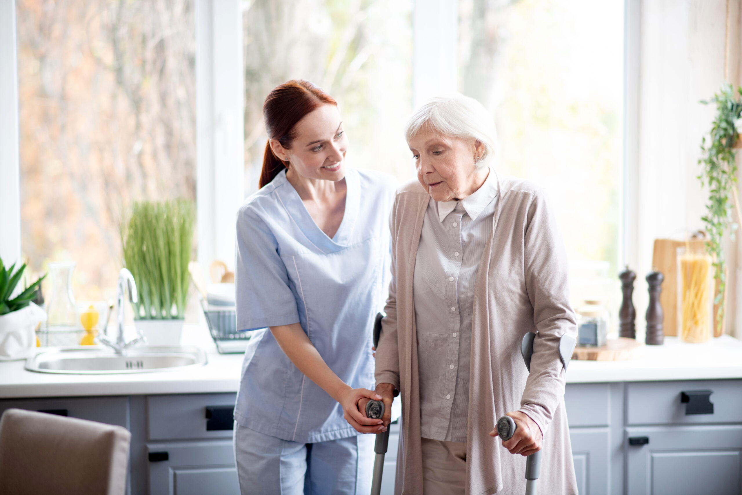 Smiling Caregiver Helping Aged Woman To Make Steps